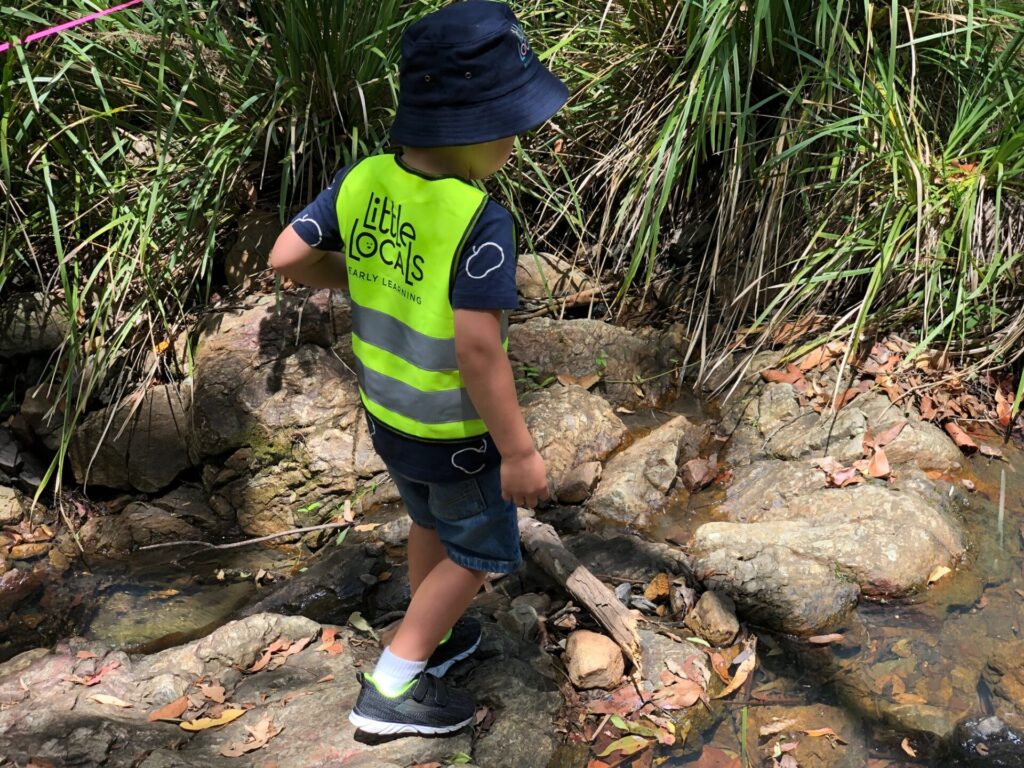 A child wearing a Little Locals’ Early Learning high-vis vest walks on a rocky surface during a Bush Kindy excursion at the long daycare centre.